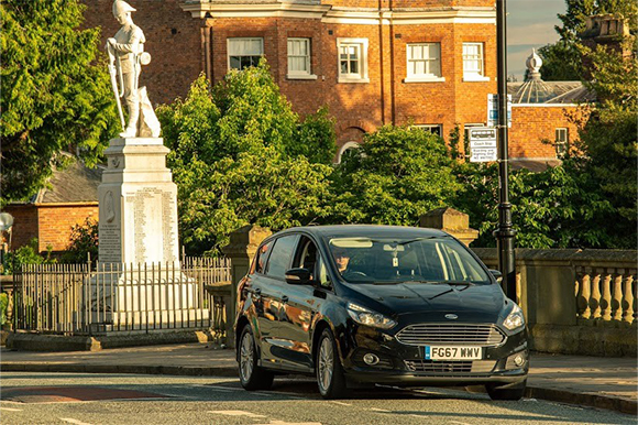 ford car parked up on street, driver in car with statue in the background