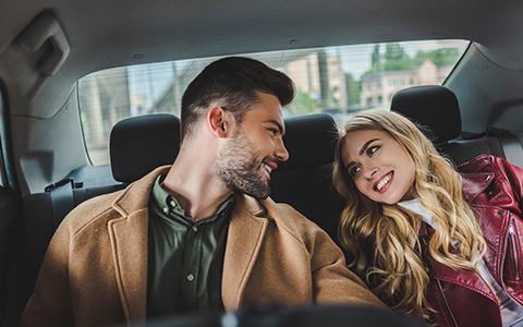 Man and woman smiling to each other, sitting in the back of a car