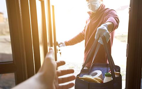 Man with gloves and mask on handing bag of shipping through a door
