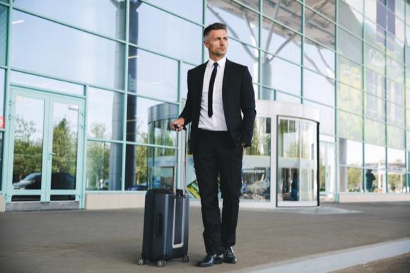 business man in suit rolling suitcase out of glass building